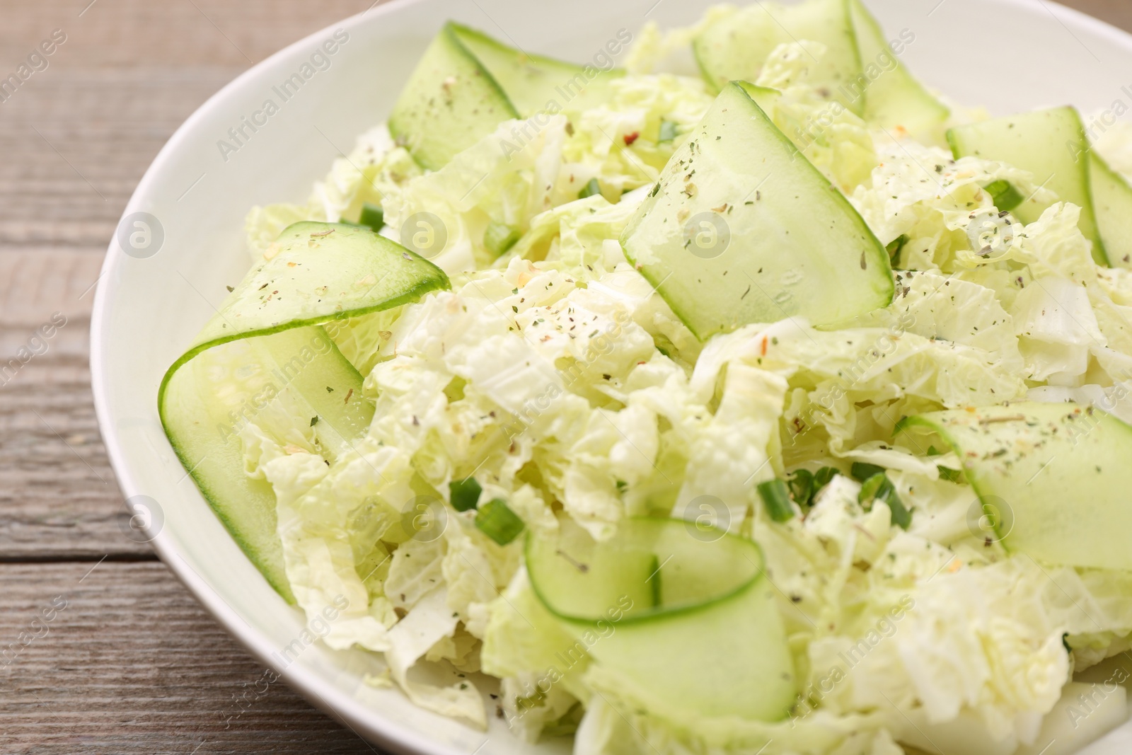 Photo of Tasty salad with Chinese cabbage, cucumber and green onion in bowl on wooden table, closeup