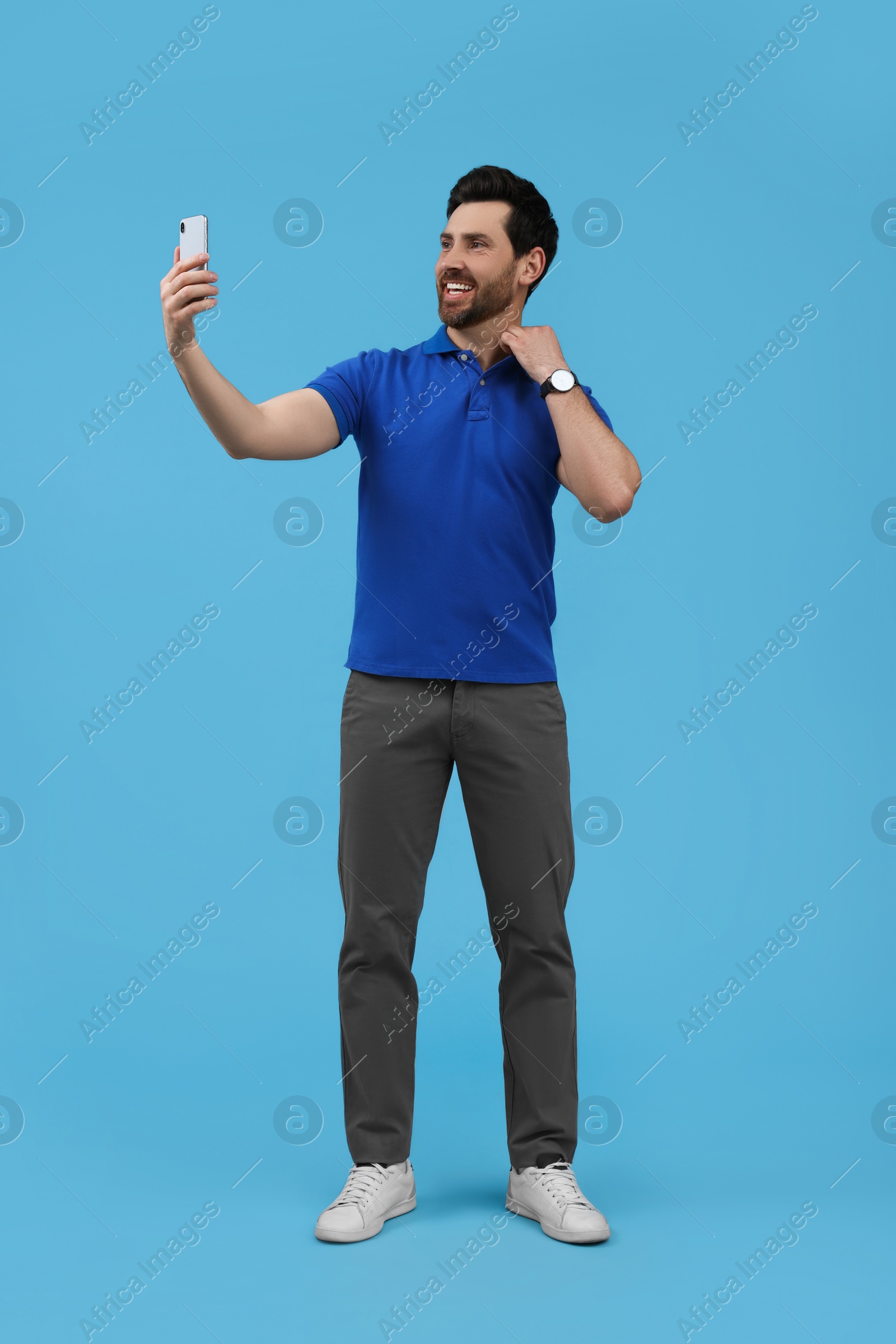 Photo of Smiling man taking selfie with smartphone on light blue background