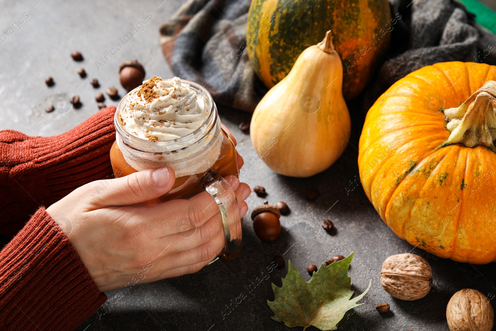 Photo of Woman holding mason jar of tasty pumpkin spice latte at grey table, closeup