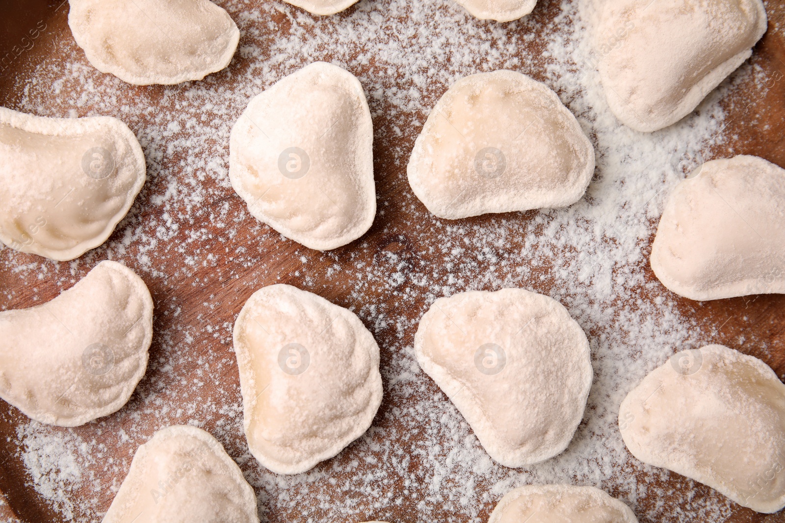 Photo of Raw dumplings (varenyky) with tasty filling and flour on wooden table, flat lay