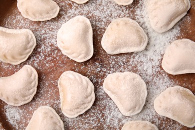 Raw dumplings (varenyky) with tasty filling and flour on wooden table, flat lay