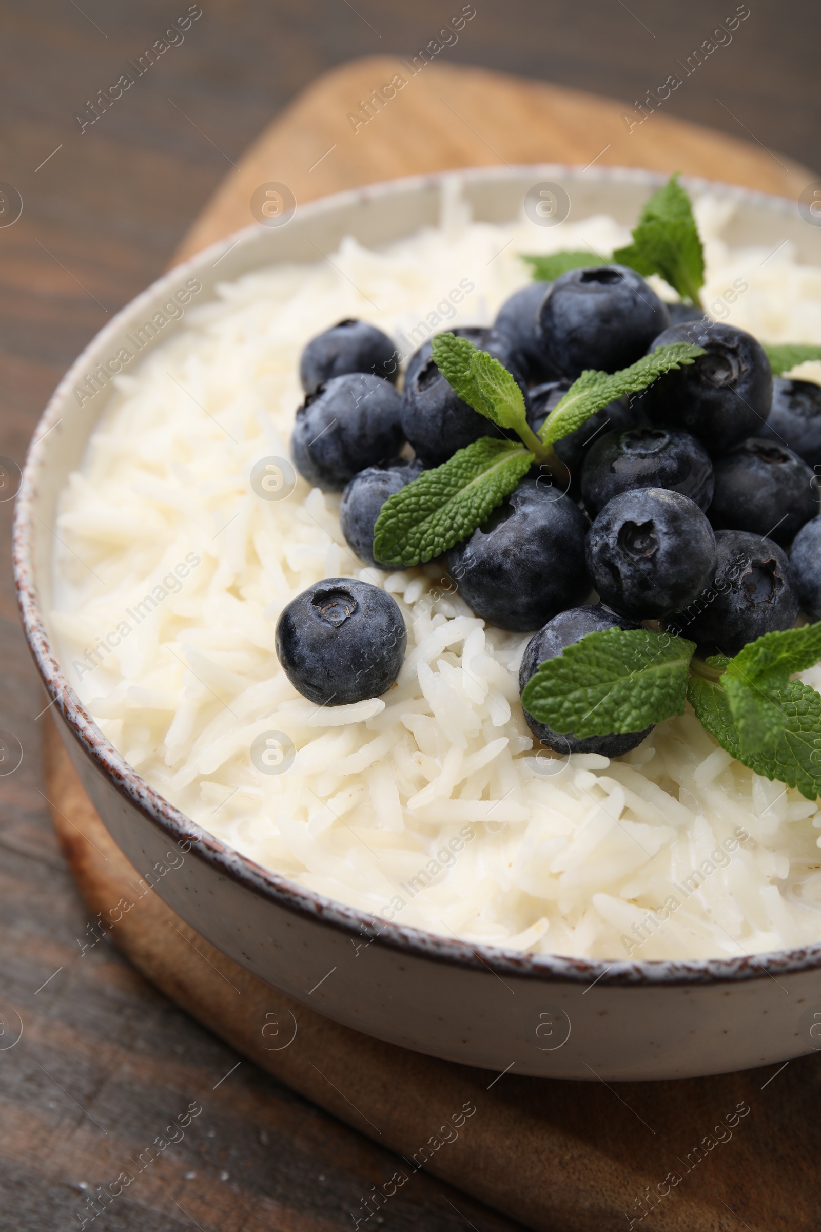 Photo of Bowl of delicious rice porridge with blueberries and mint on table, closeup