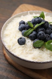 Photo of Bowl of delicious rice porridge with blueberries and mint on table, closeup