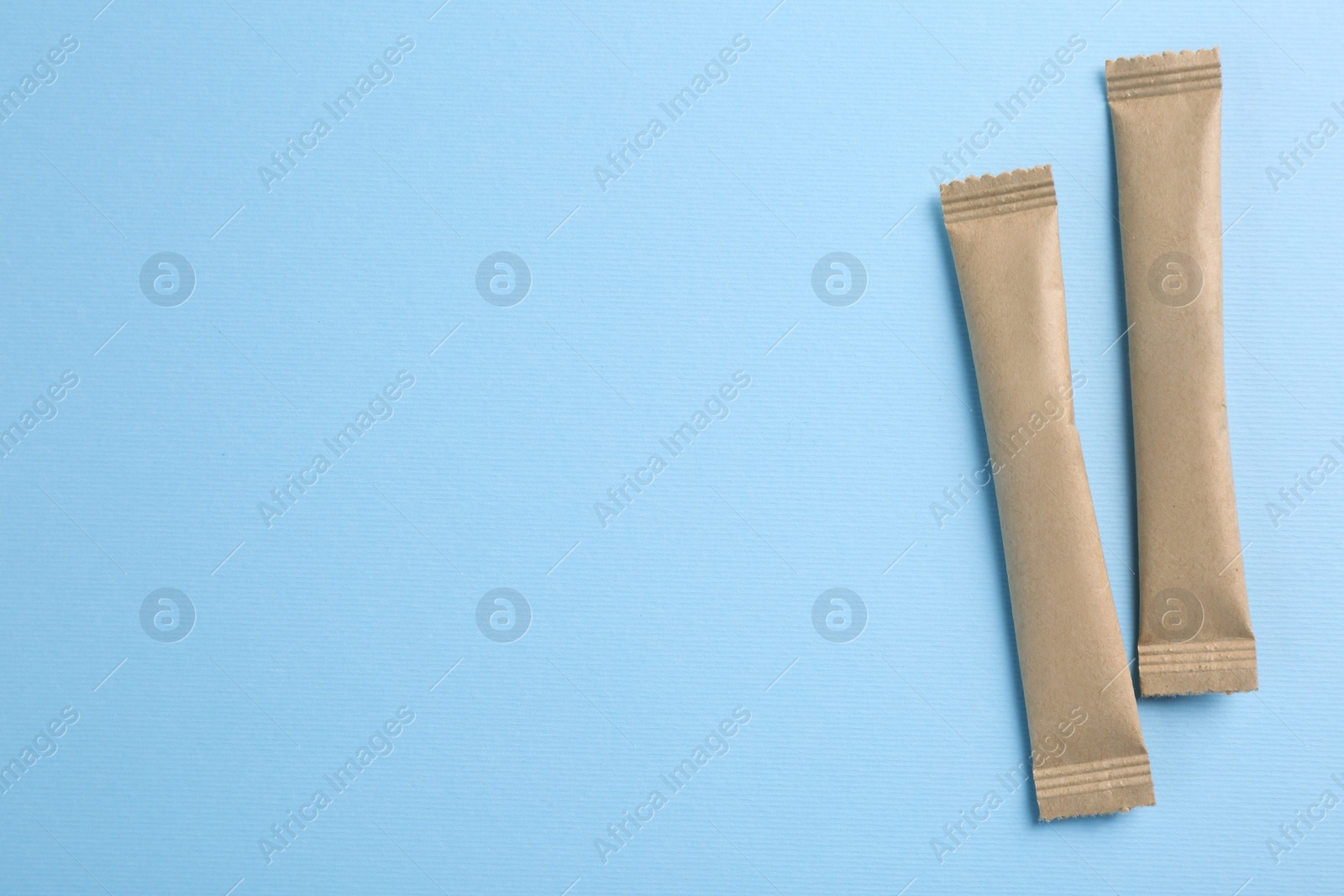 Photo of Beige sticks of sugar on light blue background, flat lay. Space for text