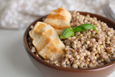 Photo of Tasty buckwheat porridge with meat on white table, closeup