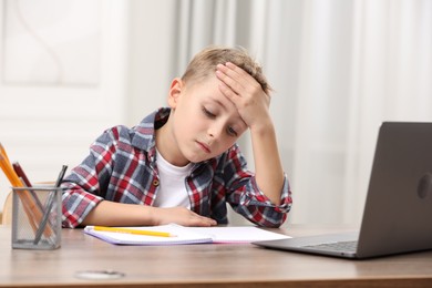 Little boy suffering from headache at wooden desk indoors