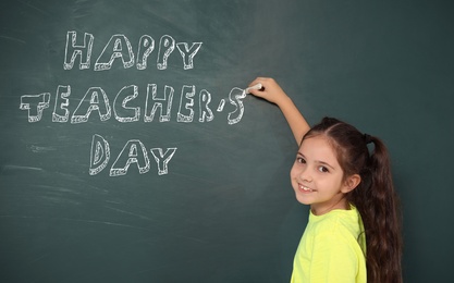 Image of Cute little girl writing phrase Happy Teacher's Day on chalkboard
