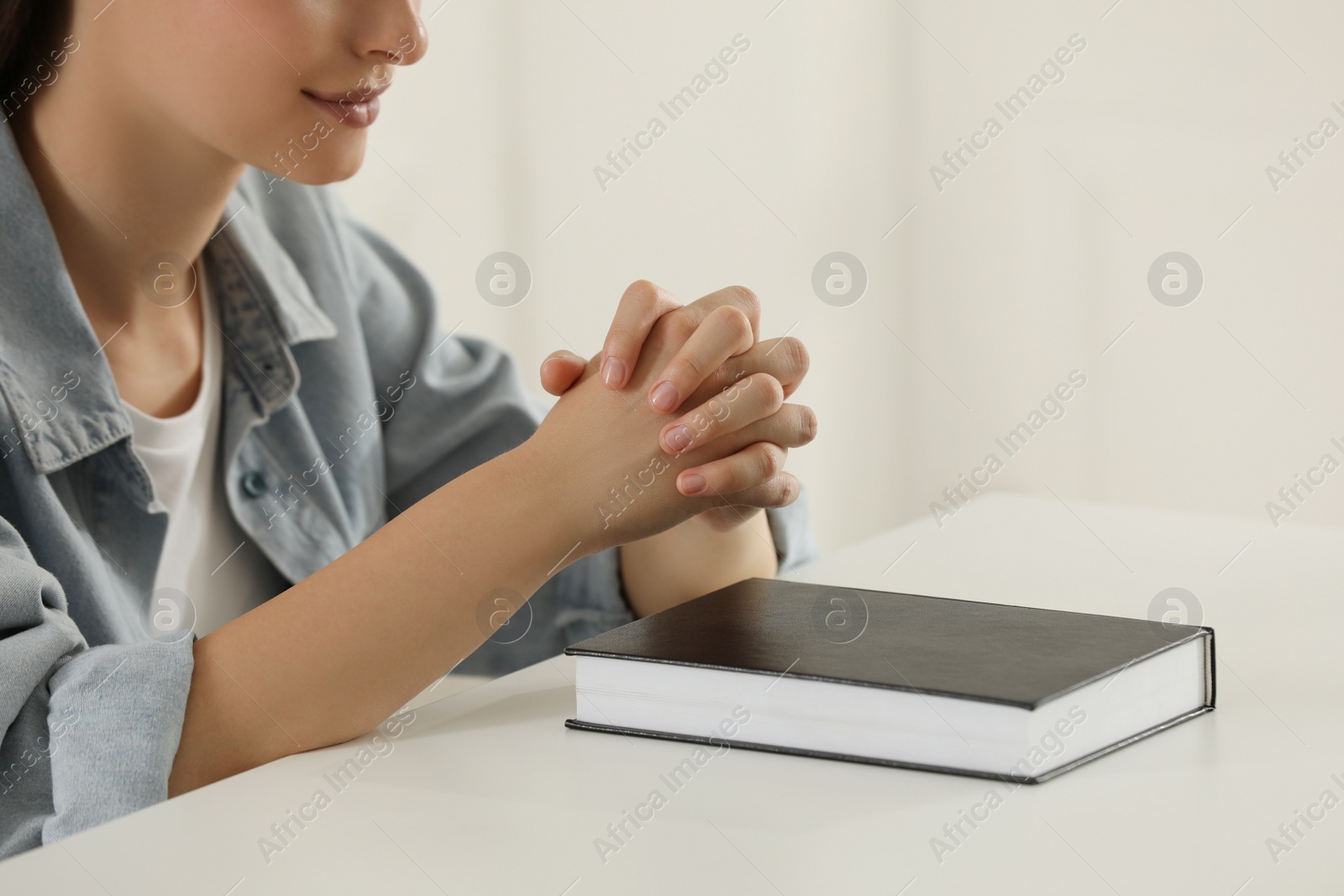 Photo of Religious woman praying over Bible at table indoors, closeup