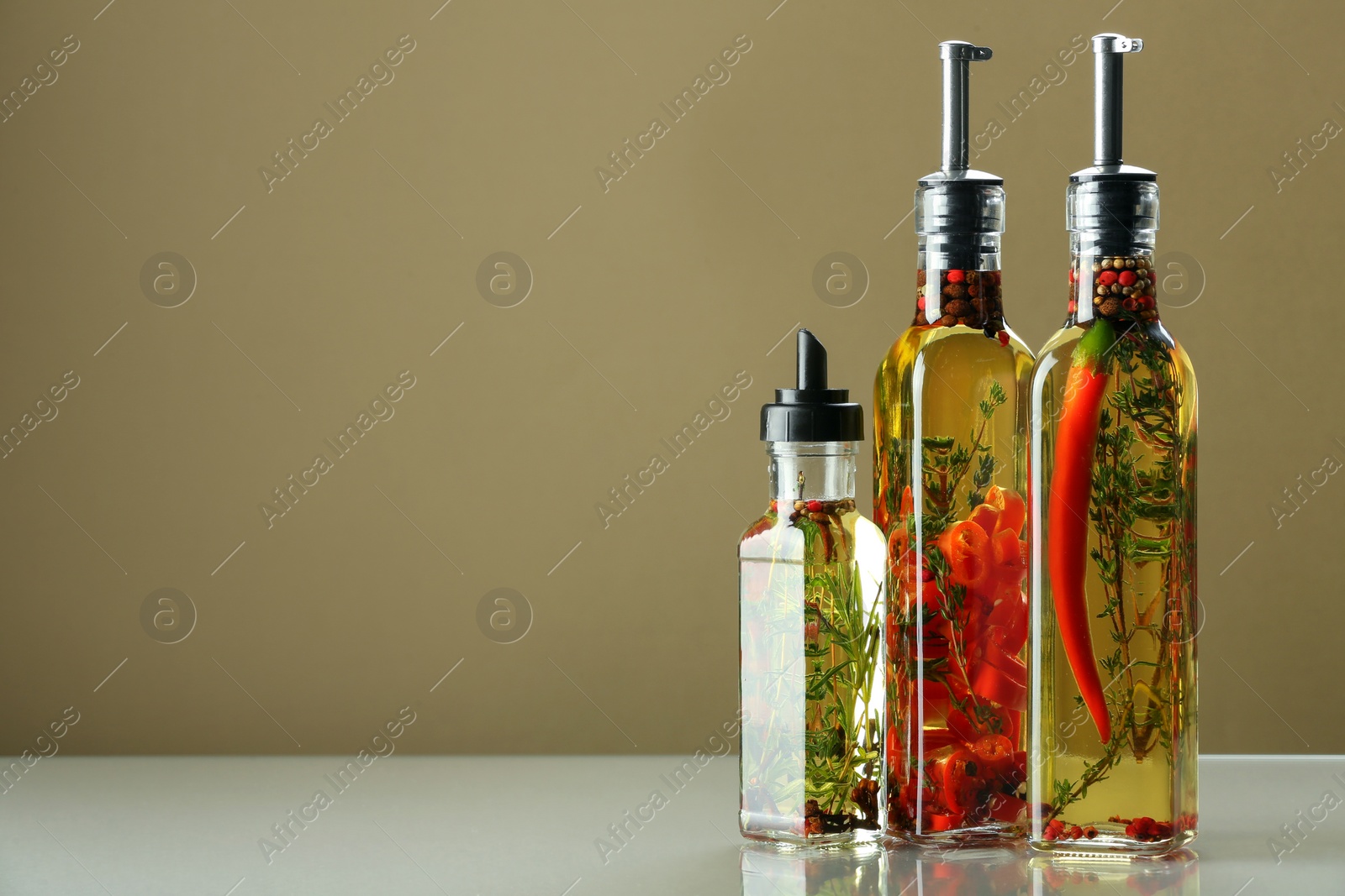 Photo of Cooking oil with different spices and herbs in bottles on beige table. Space for text