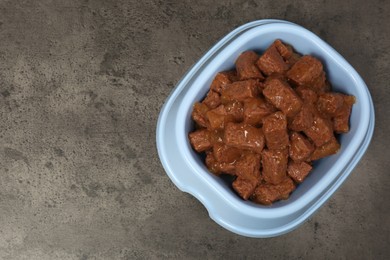 Photo of Wet pet food in feeding bowl on grey stone background, top view. Space for text