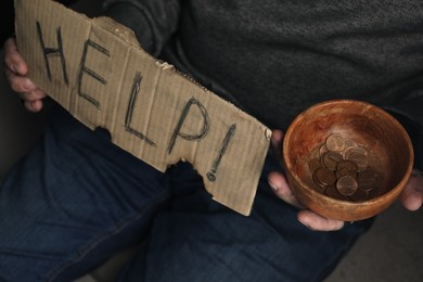 Poor homeless man with help sign holding bowl of donations, closeup