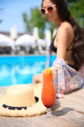 Woman with cocktail and straw hat near swimming pool