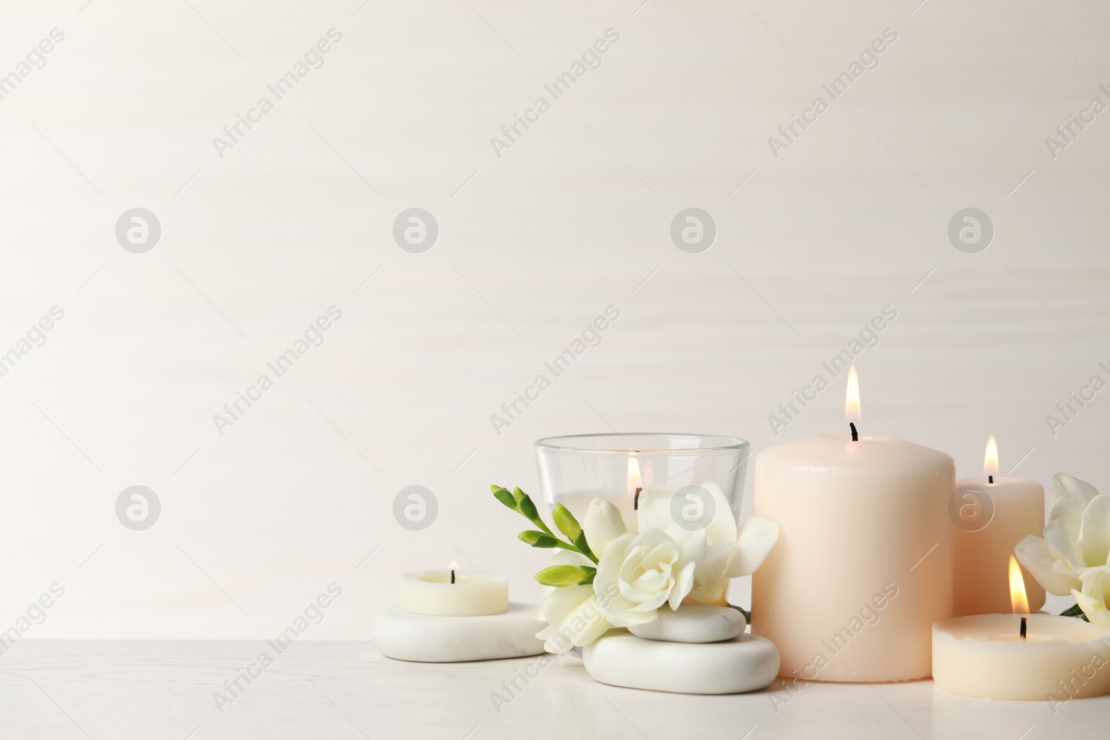 Photo of Beautiful composition with burning candles, spa stones and flowers on white table. Space for text