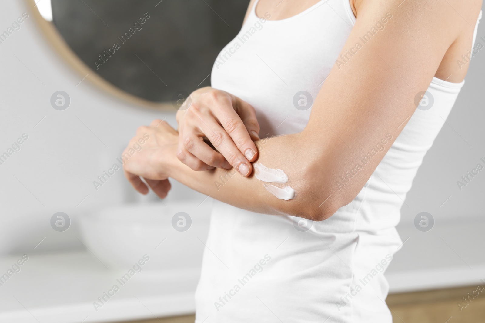 Photo of Woman applying body cream onto elbow in bathroom, closeup. Space for text