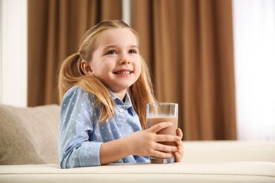 Cute little child with glass of tasty chocolate milk at home
