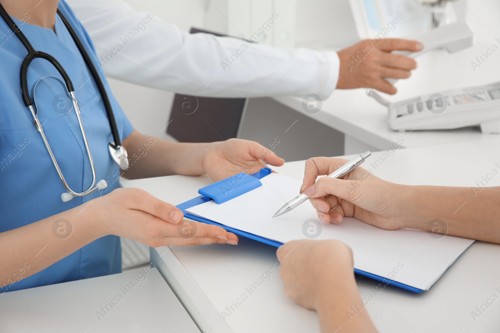 Photo of Young female doctor working with client at reception desk in hospital