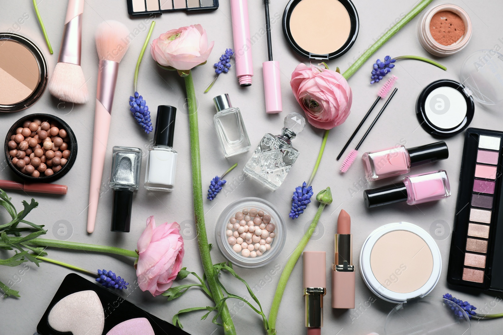 Photo of Flat lay composition with different makeup products and beautiful spring flowers on gray background