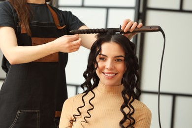 Hair styling. Hairdresser curling woman's hair in salon, closeup