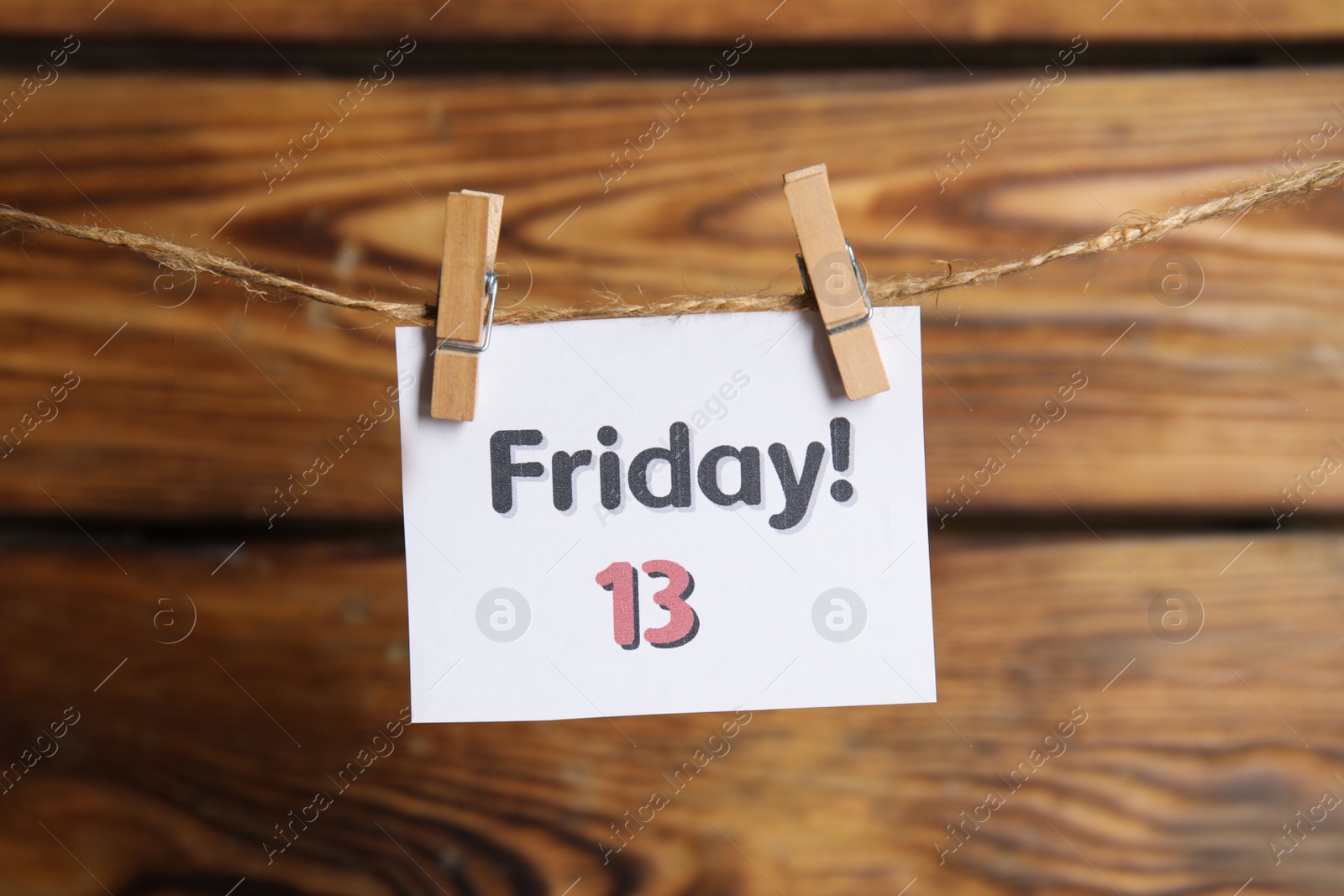 Photo of Paper note with phrase Friday! 13 hanging on twine against wooden background. Bad luck superstition