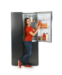 Young woman taking juice out of refrigerator on white background