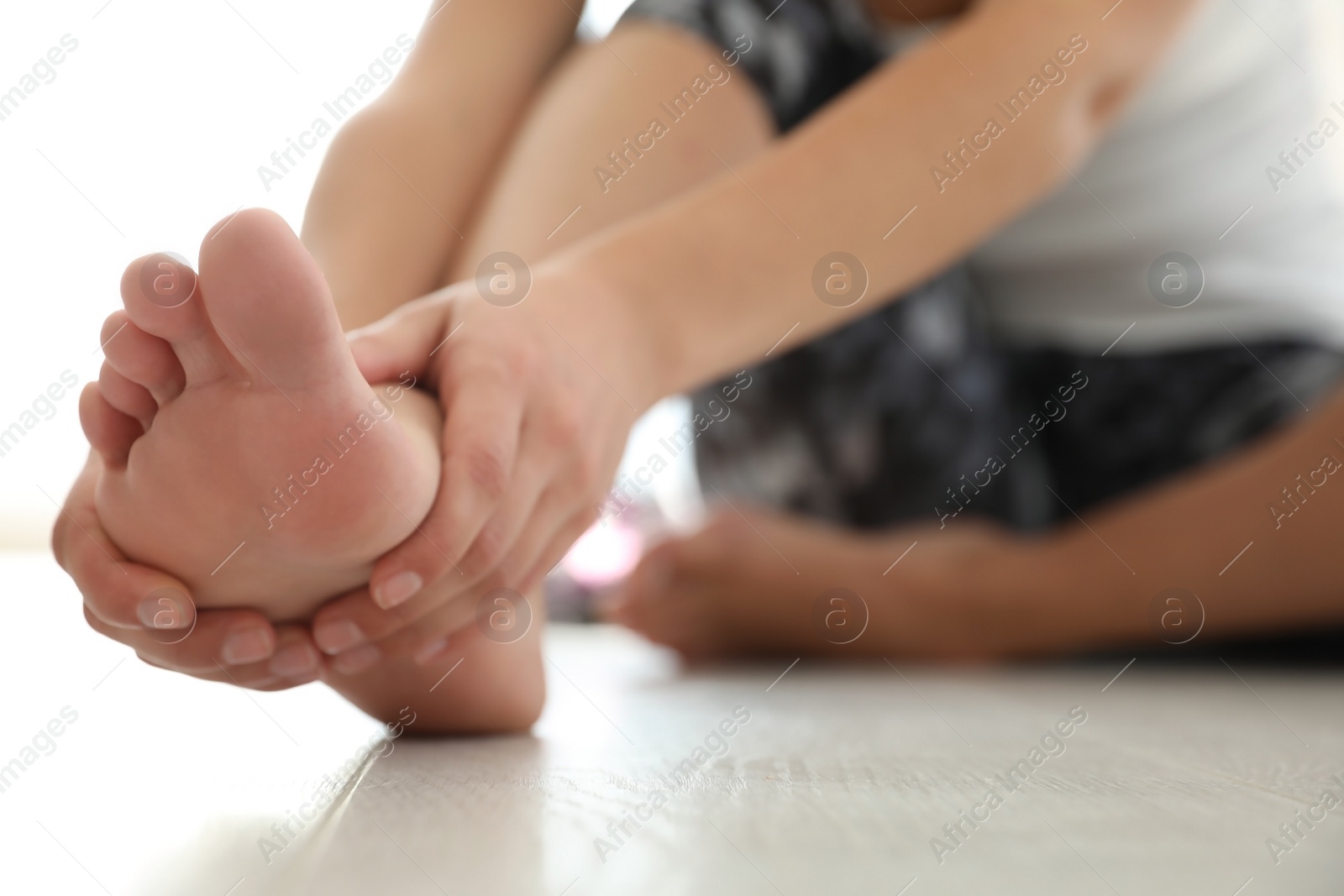 Photo of Young woman suffering from pain in foot on floor, closeup