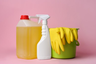 Photo of Green bucket with gloves and detergents on pink background. Cleaning supplies