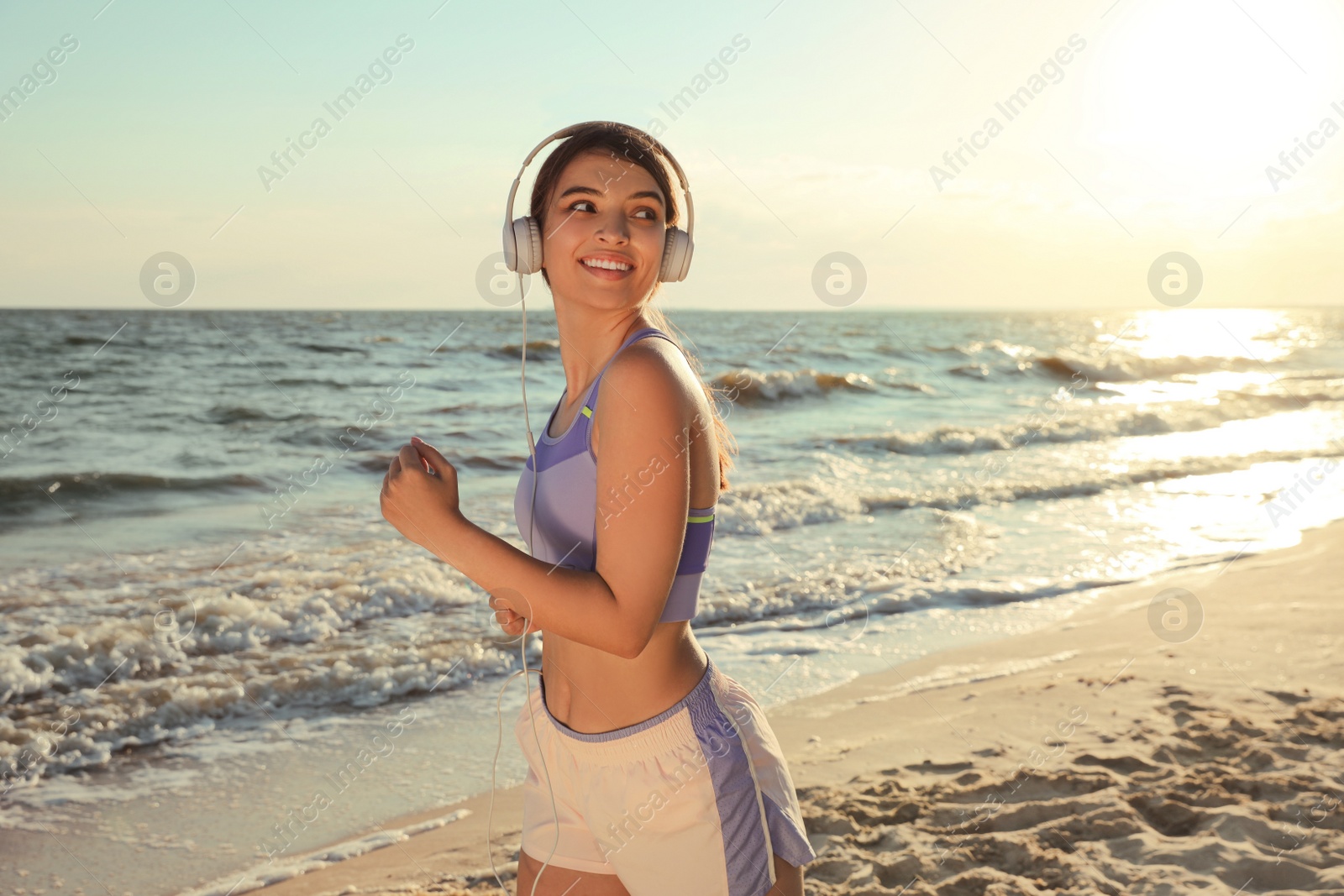 Photo of Young woman running on beach at sunset
