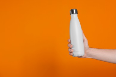 Man holding thermo bottle with drink on orange background, closeup. Space for text