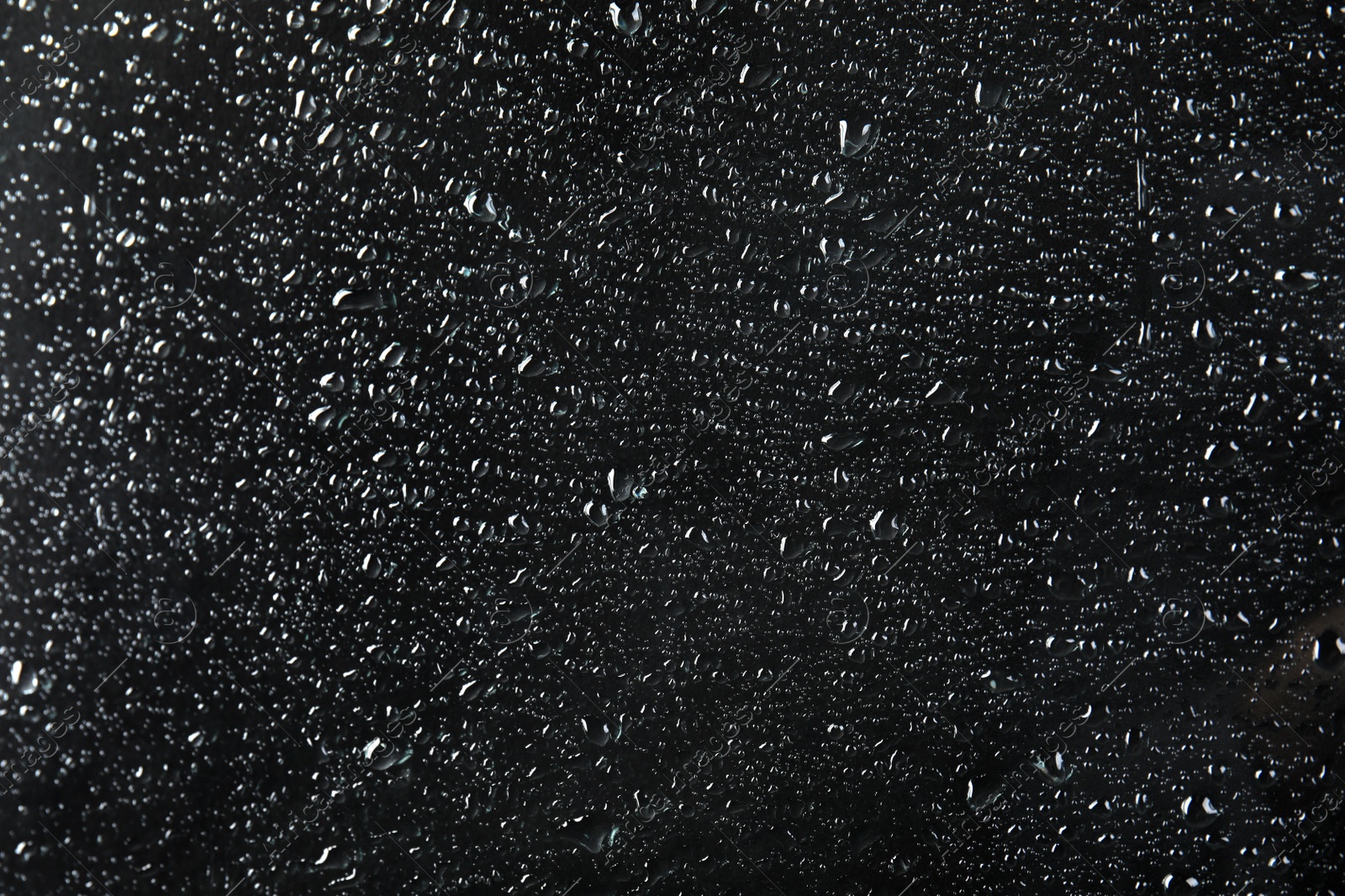 Photo of Glass with rain drops against dark background