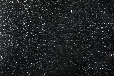 Photo of Glass with rain drops against dark background