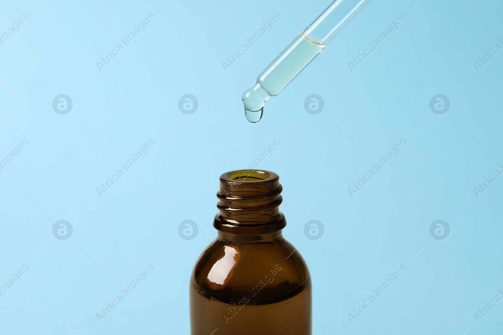 Photo of Dripping cosmetic oil from pipette into bottle on light blue background, closeup
