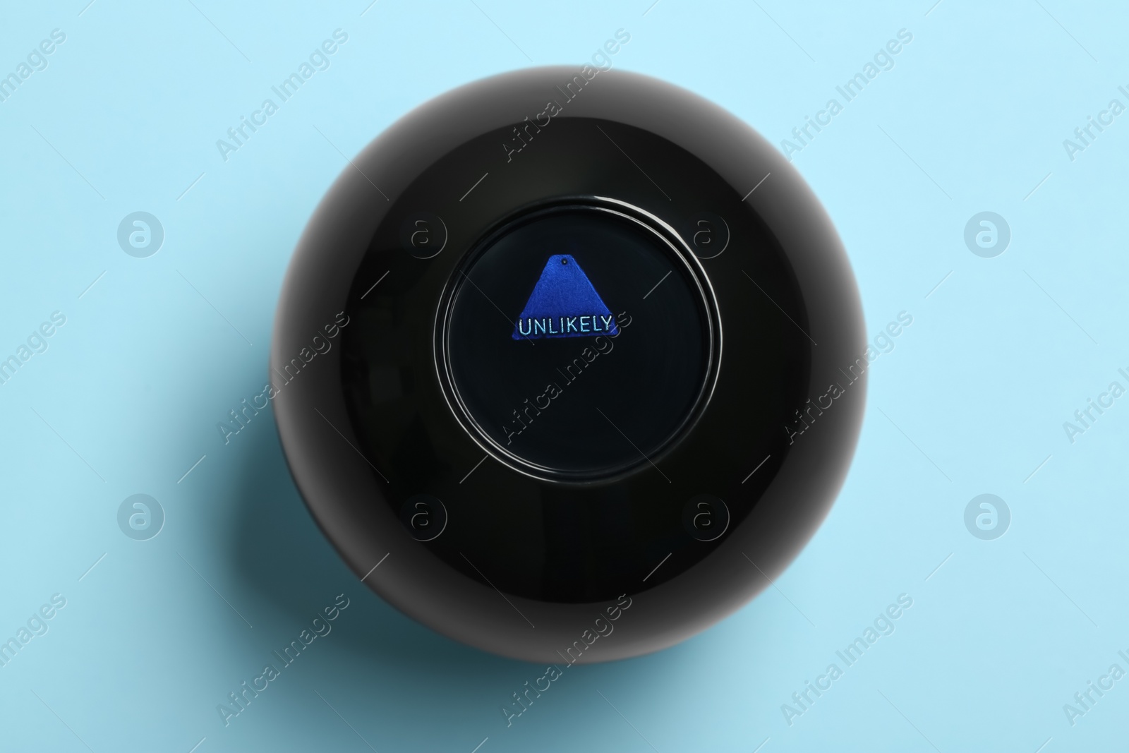 Photo of Magic eight ball with prediction Unlikely on light blue background, top view