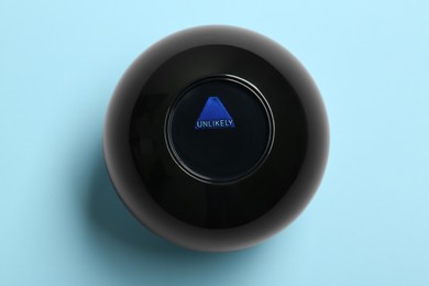 Photo of Magic eight ball with prediction Unlikely on light blue background, top view