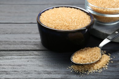 Brown sugar in bowls and spoon on black wooden table, closeup. Space for text