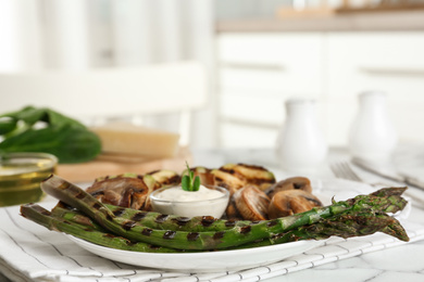 Photo of Tasty grilled asparagus served with sauce and mushrooms on table