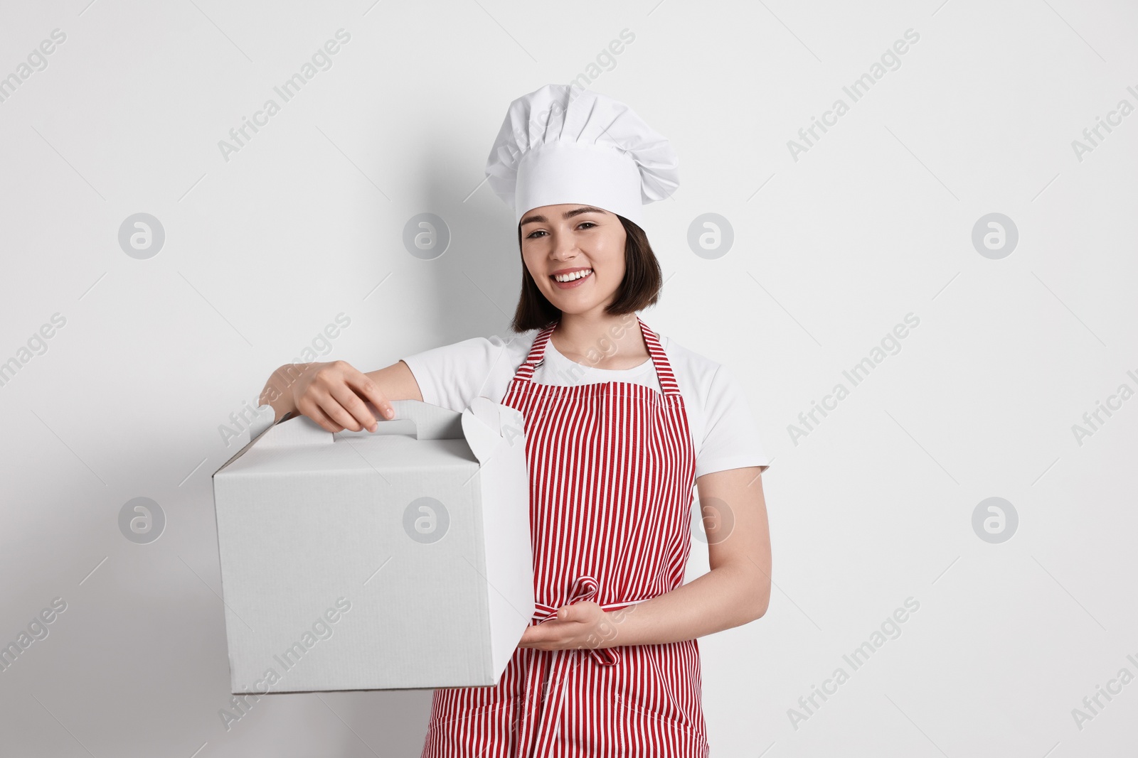 Photo of Happy confectioner with cake box on light grey background