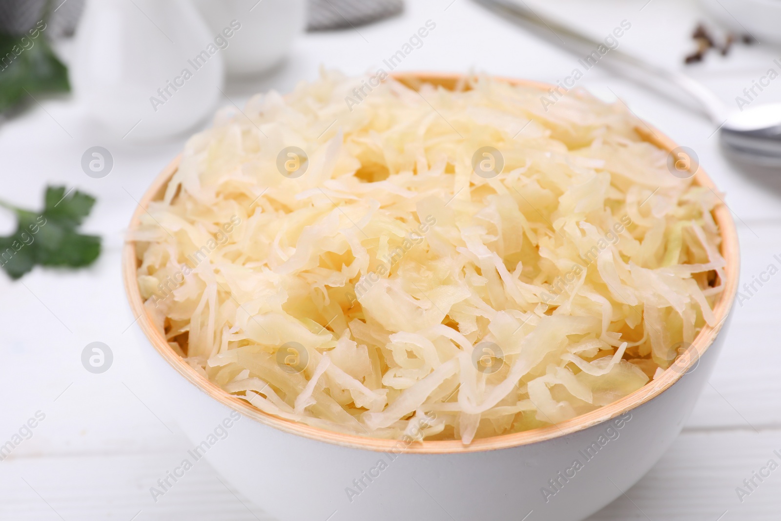 Photo of Bowl of tasty sauerkraut on white wooden table, closeup