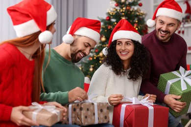 Photo of Christmas celebration in circle of friends. Happy woman and man opening gifts at home