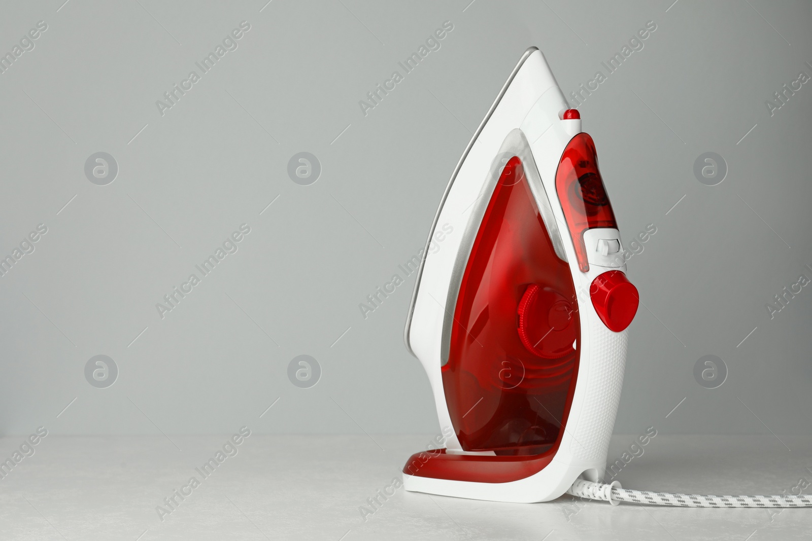 Photo of One modern iron on light grey background, space for text. Home appliance