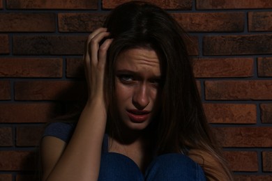 Abused young woman crying near brick wall. Domestic violence concept