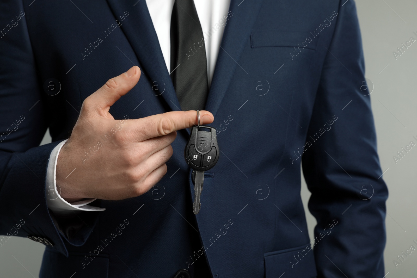 Photo of Young man holding car key on grey background, closeup