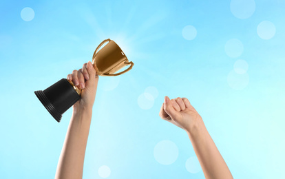 Image of Woman holding gold trophy cup on light blue background, closeup