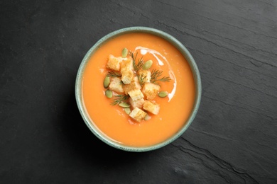 Photo of Delicious pumpkin soup in bowl on black table, top view