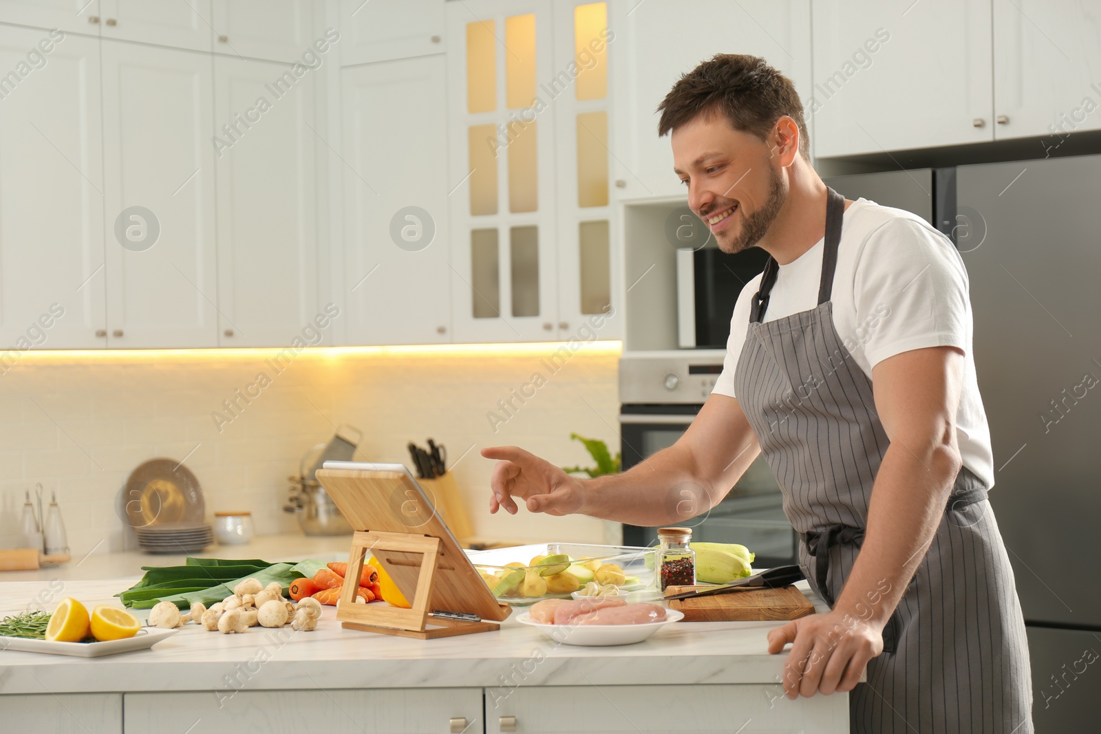 Photo of Man watching online cooking course via tablet in kitchen