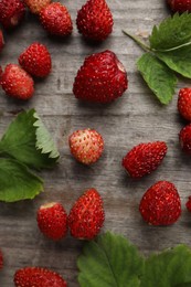 Many fresh wild strawberries and leaves on wooden table, flat lay