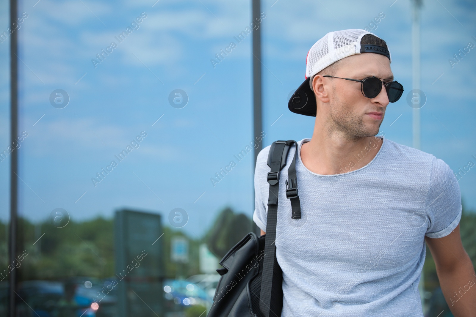 Photo of Handsome young man with stylish sunglasses and backpack near reflection surface outdoors, space for text