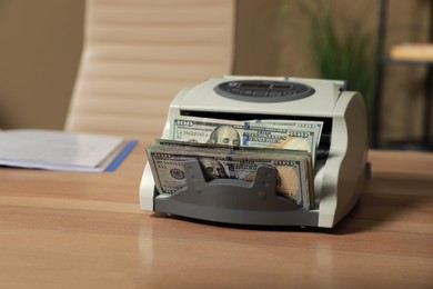 Photo of Modern banknote counter with money on wooden table indoors