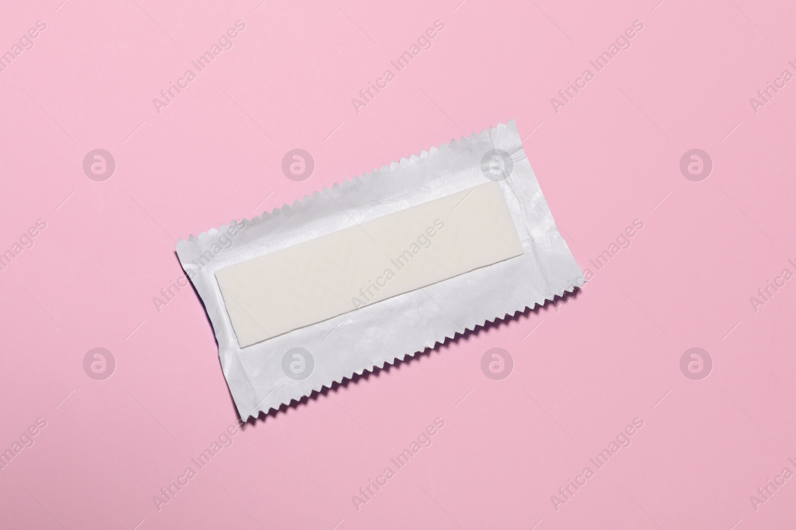 Photo of Unwrapped stick of tasty chewing gum on pink background, top view