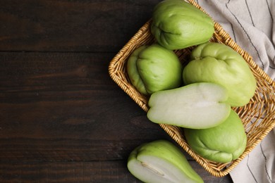 Cut and whole chayote in wicker basket on wooden table, flat lay. Space for text