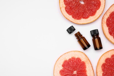 Photo of Bottles of citrus essential oil and fresh grapefruit slices on white background, flat lay. Space for text